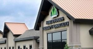 Northwoods Therapy Associates office building with beige siding and black-trimmed windows under a cloudy sky