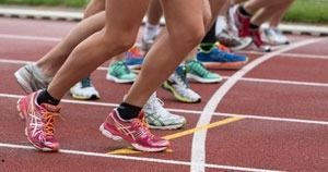 Runners' legs lined up at the starting line on a track, wearing colorful shoes.
