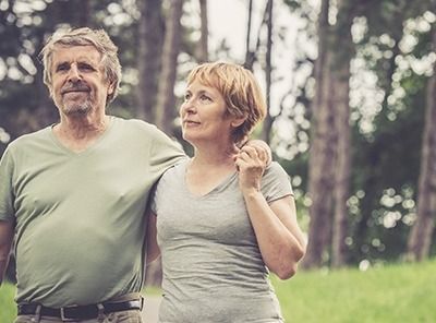 Two people standing arm in arm in a park, looking ahead with a calm expression.