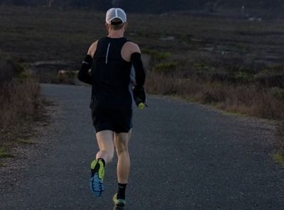 Runner in black athletic gear jogging along a paved path at dusk