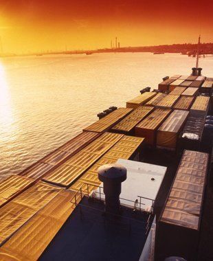 A large ship filled with containers is docked in the water at sunset