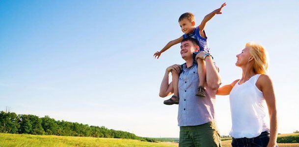 A man and woman are carrying a child on their shoulders in a field.