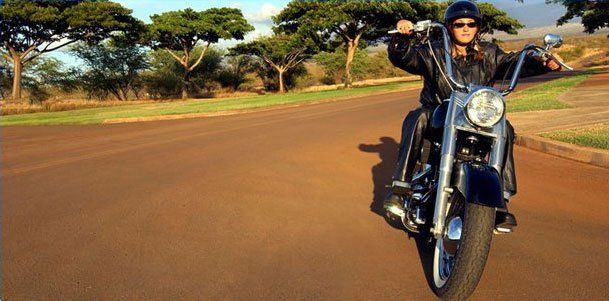 A woman is riding a motorcycle down a dirt road.