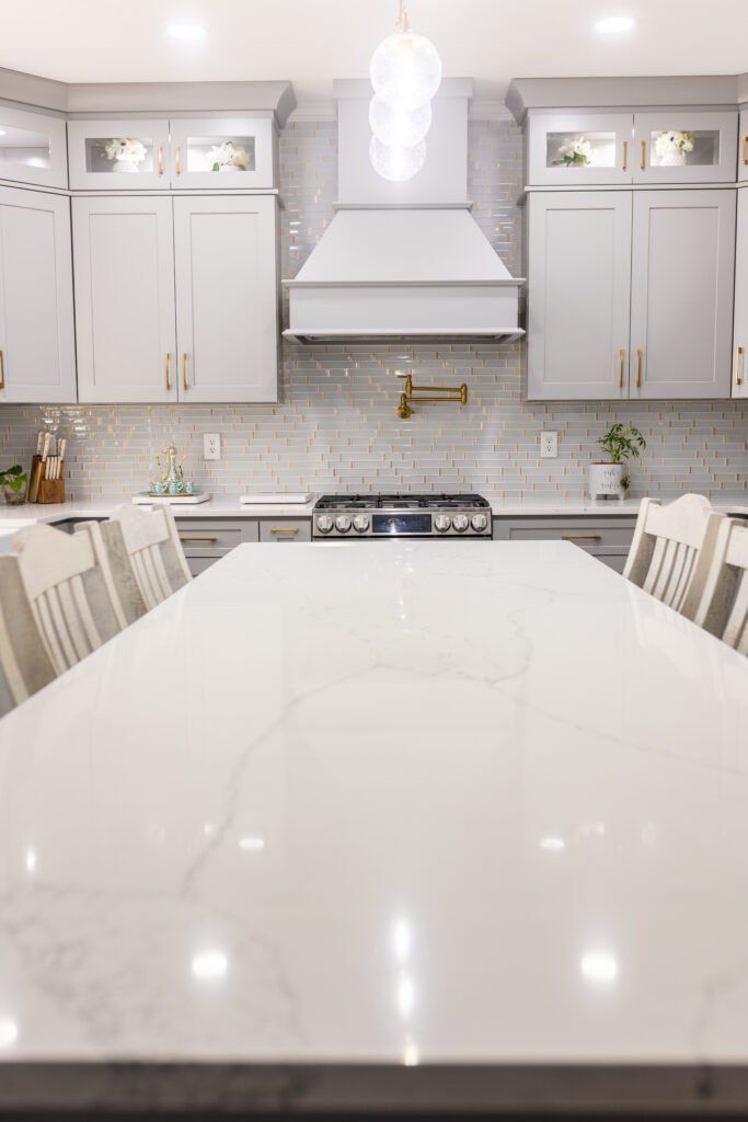 Bright modern kitchen with white island, cabinets, marble backsplash, and stainless steel stove hood