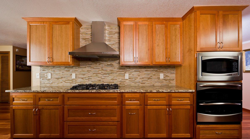 Warm wood kitchen with stainless steel range hood, stove, double oven, and tiled backsplash