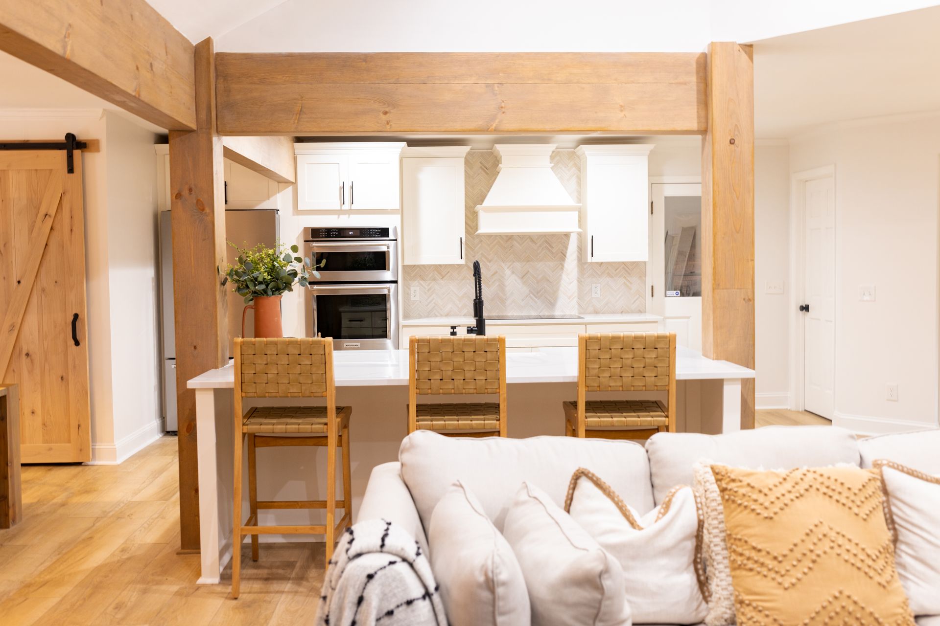 Bright open-plan kitchen and living room with wood beams, island stools, and beige sofa in foreground