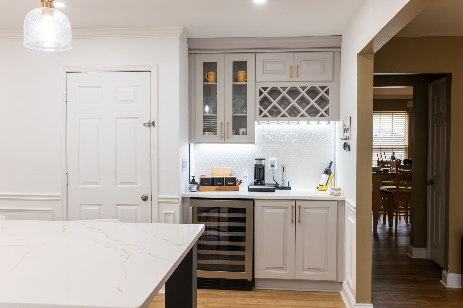 Bright modern kitchen with white cabinets, wine cooler, island, and an open doorway to a dining room