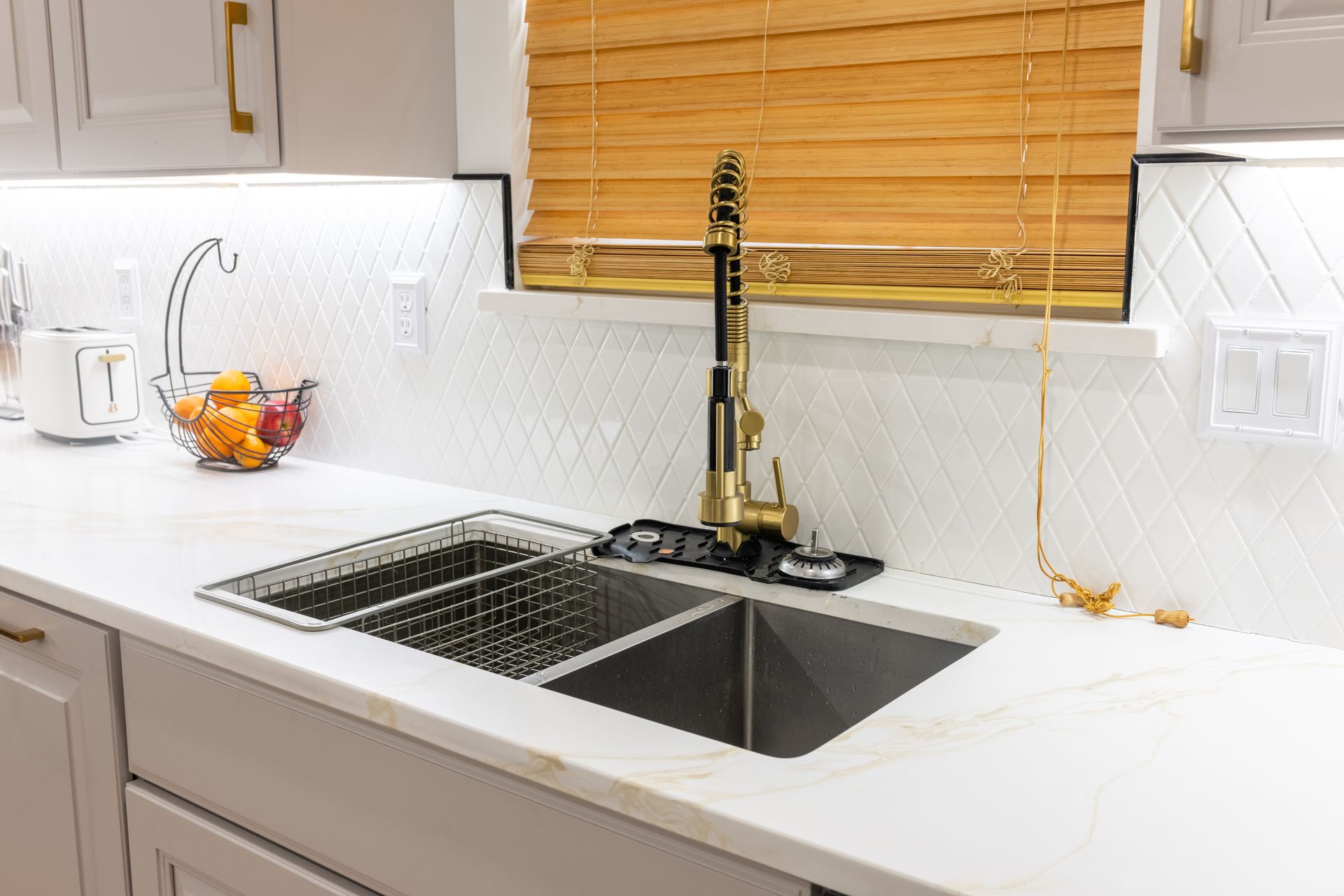 Modern kitchen sink with white countertops, brass faucet, and bamboo window blinds