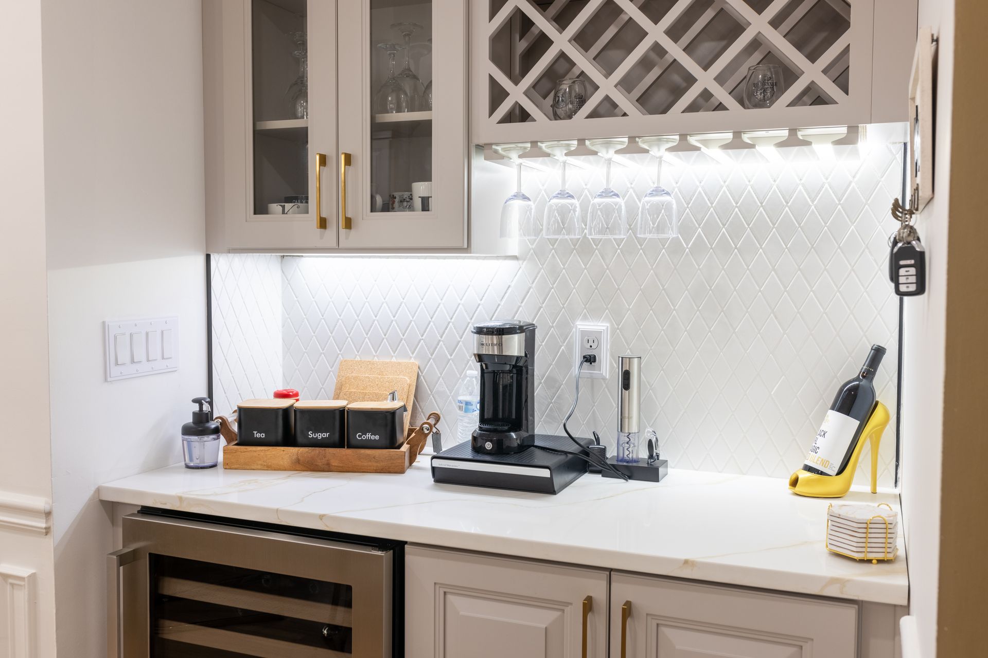 Modern kitchen counter with coffee maker, wine rack, and small appliances under under-cabinet lighting