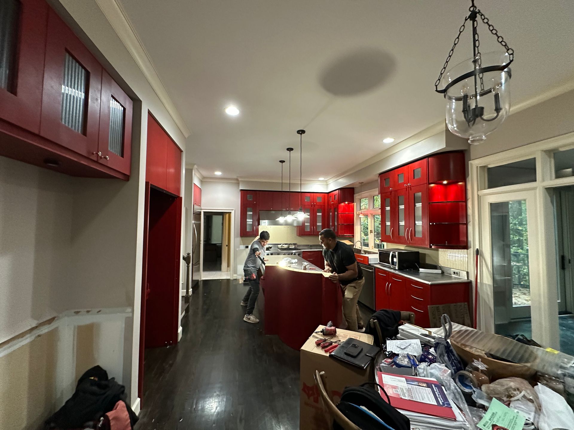 Bright kitchen with red cabinets, dark floors, and two people standing at the island.