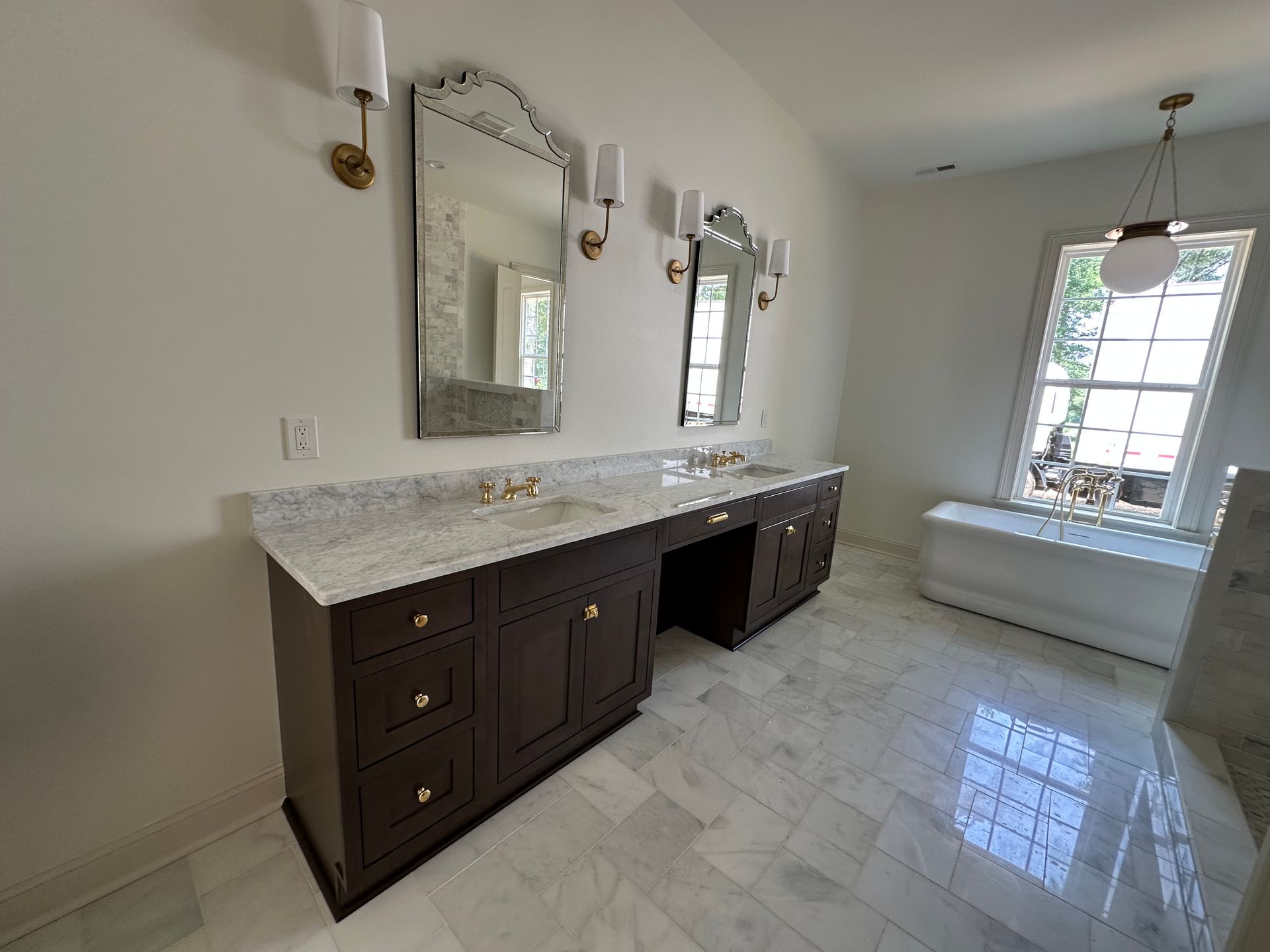 Bright bathroom with double vanity, marble countertop, mirrors, and large windowed tub area.