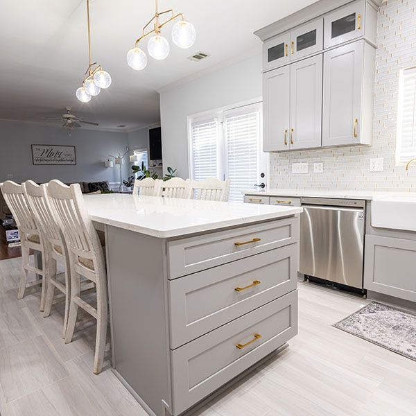 Bright modern kitchen with white island, gray cabinets, pendant lights, and dining chairs.