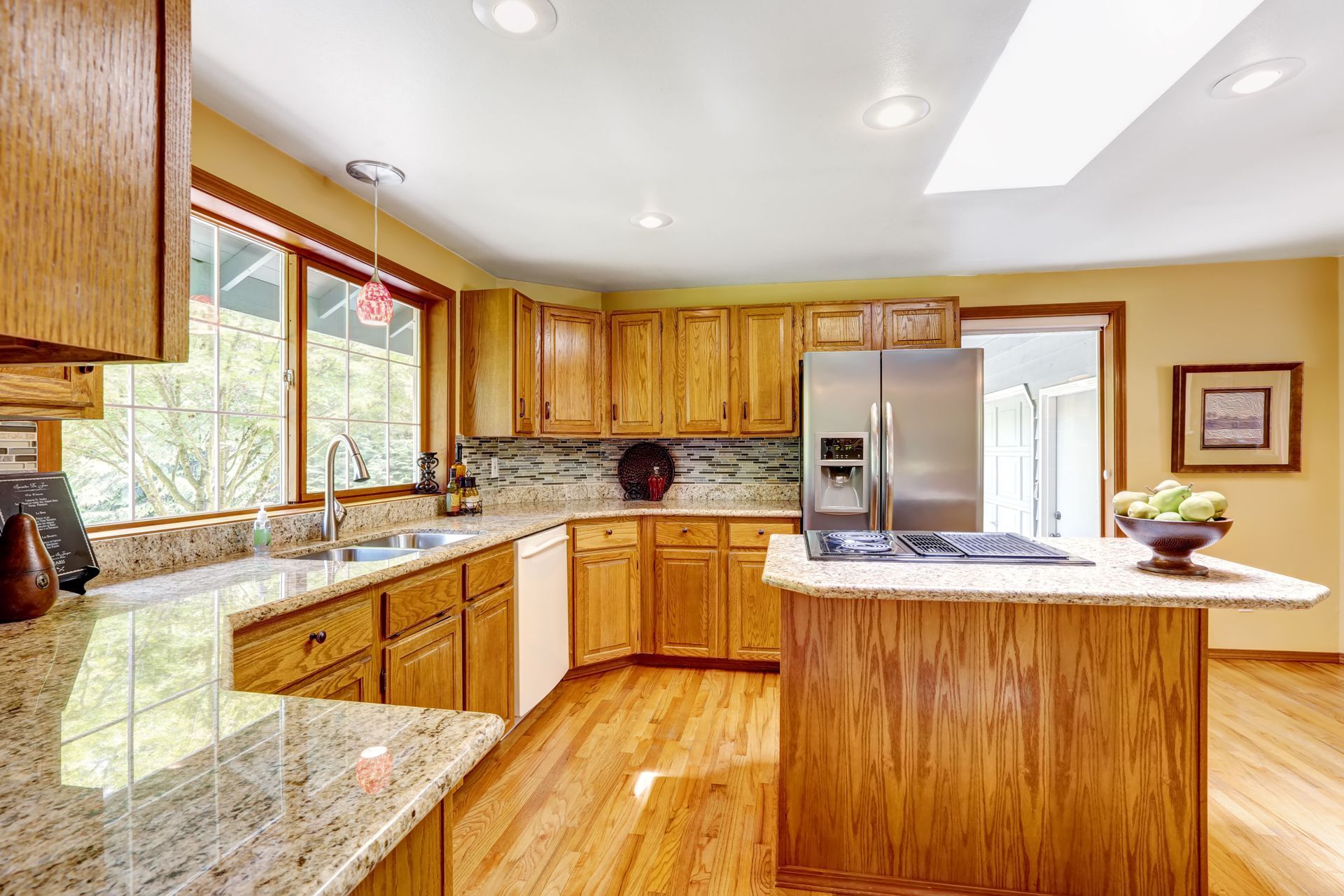 Bright kitchen with wood cabinets, granite counters, stainless steel fridge, and a central island.