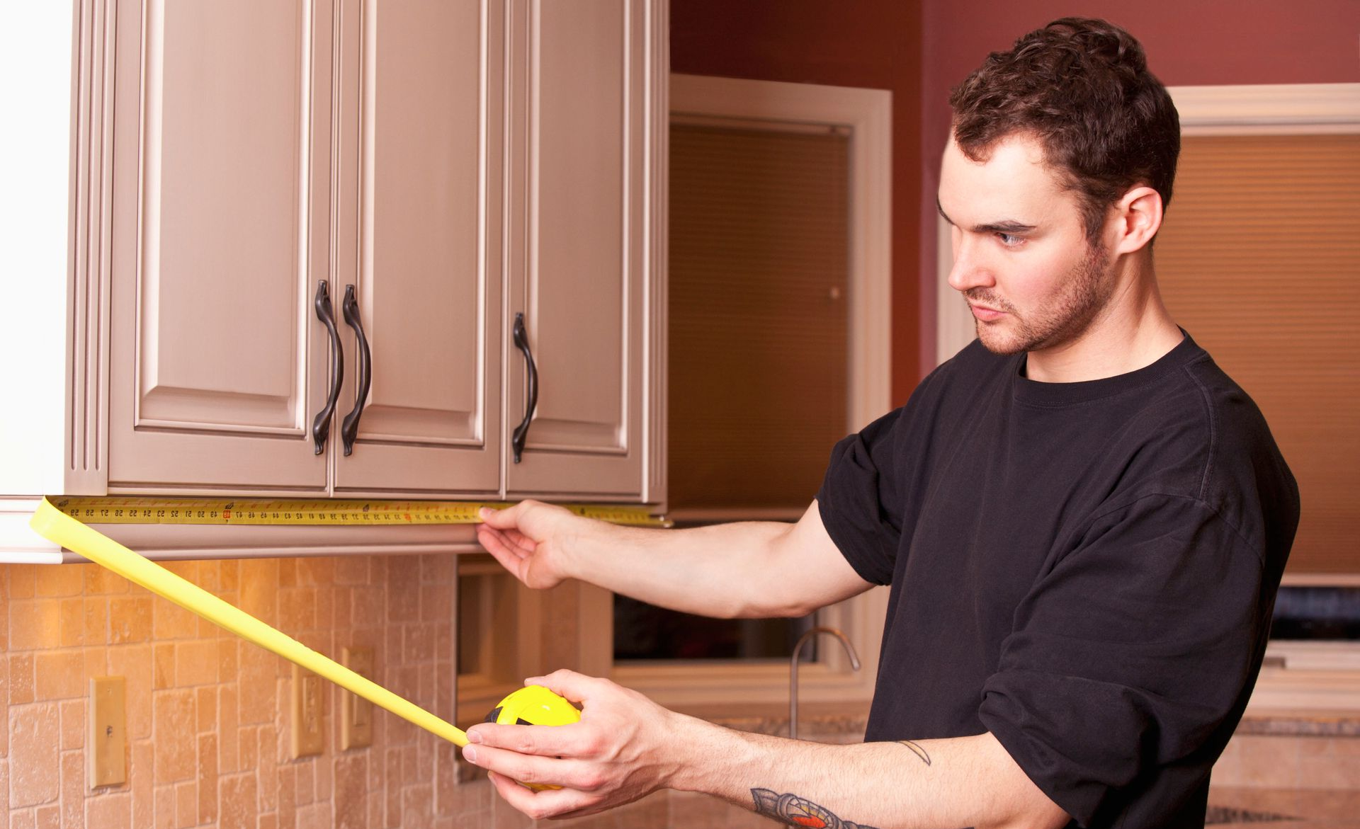 Man measuring kitchen cabinet height with a yellow tape measure