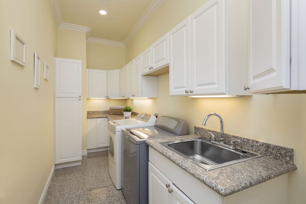 Narrow kitchen with white cabinets, granite counters, sink, and stove along a beige wall.