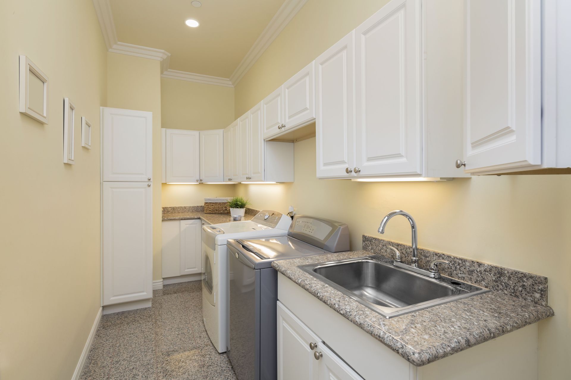 Narrow kitchen with white cabinets, granite counters, sink, and stove along a beige wall.