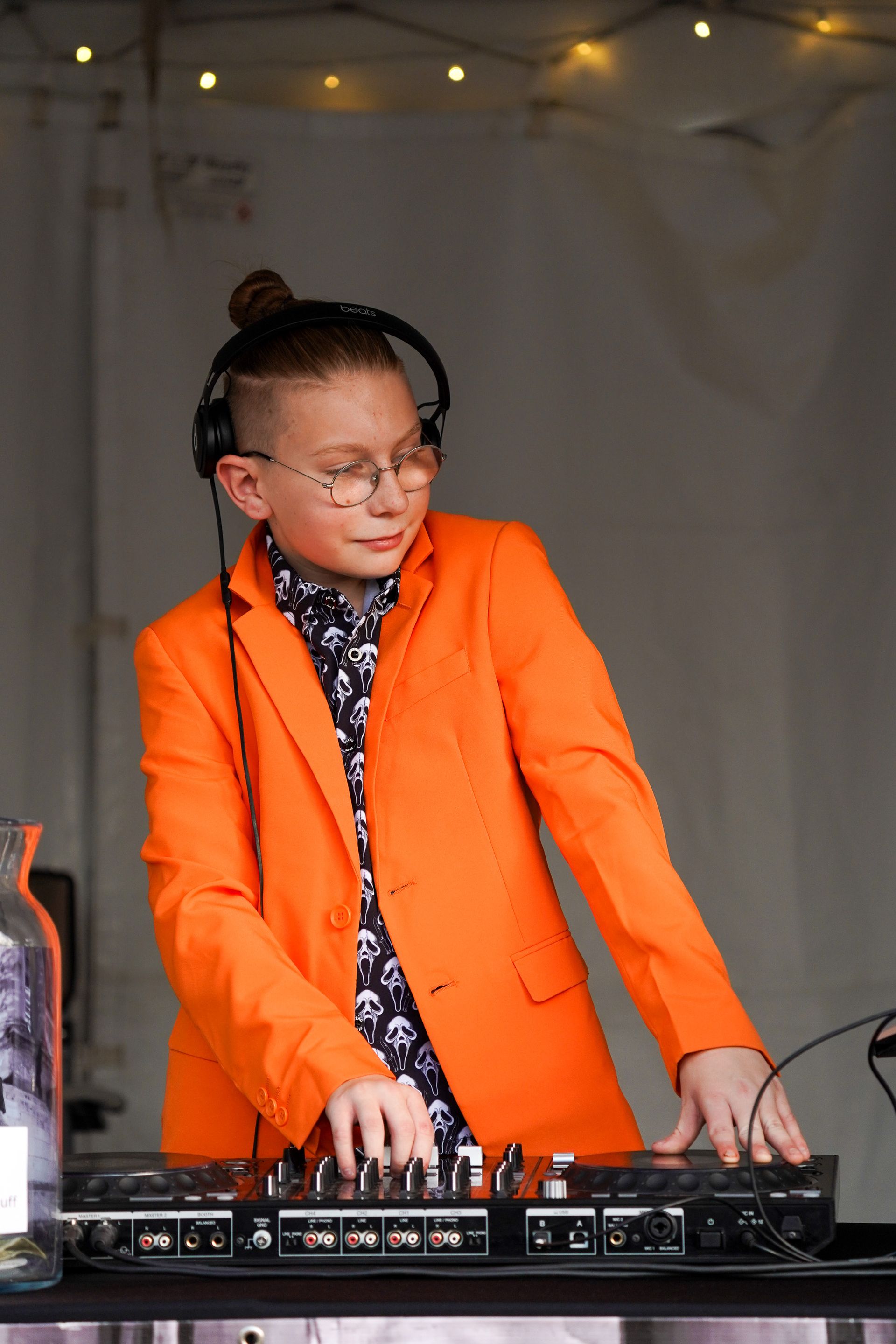 a young boy in an orange jacket and headphones is playing music on a dj controller