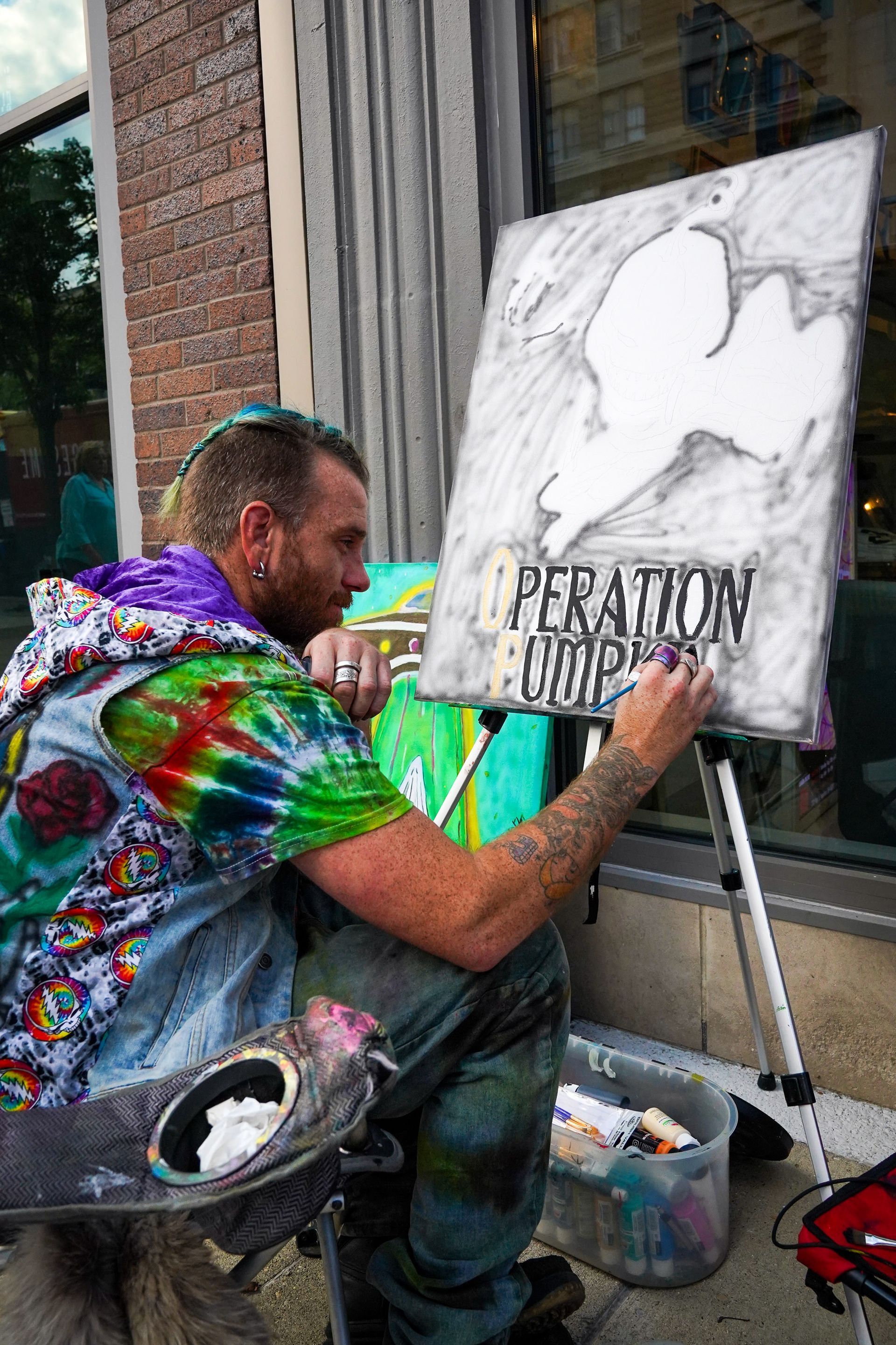 a man in a tie dye shirt is painting a picture on an easel
