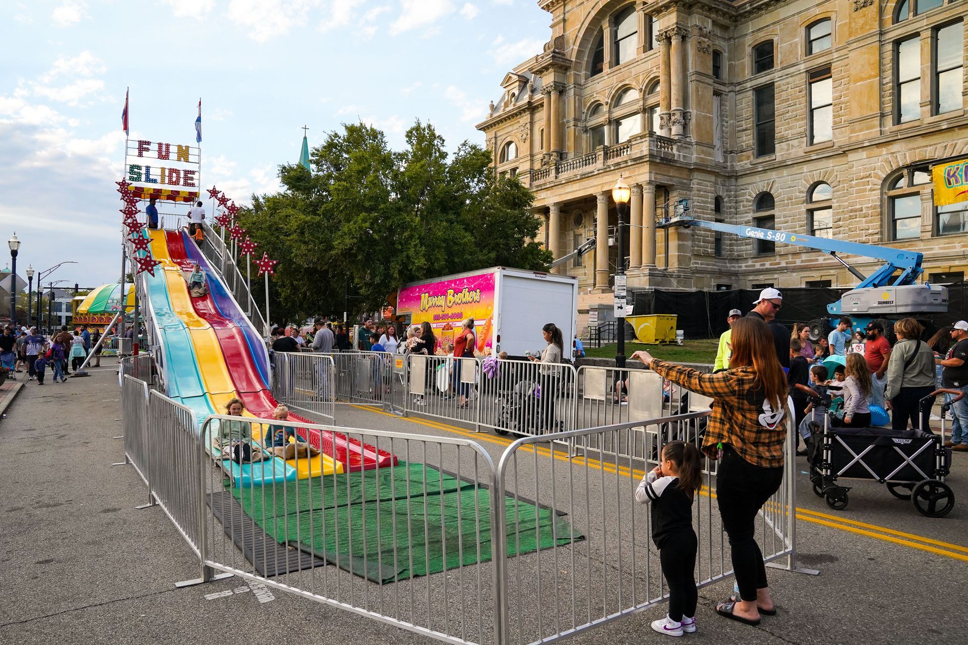 a woman and child are standing in front of a water slide at a carnival