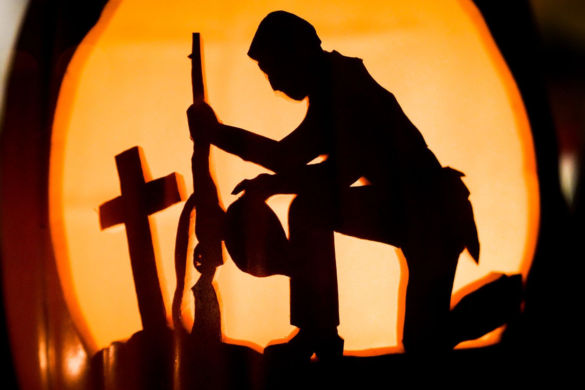 a pumpkin with a silhouette of a soldier kneeling in front of a cross