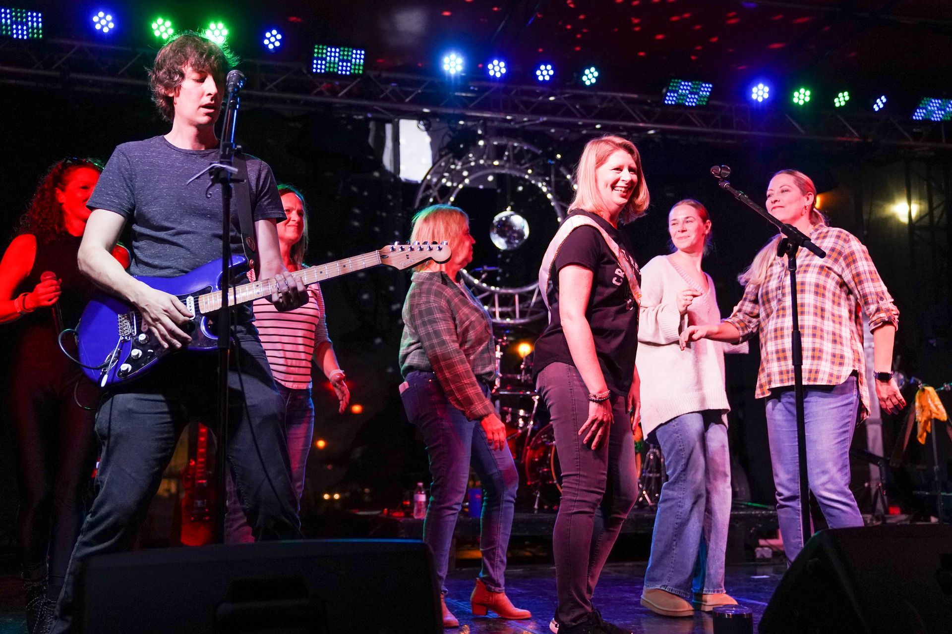 a group of people are standing on a stage with a man playing a guitar