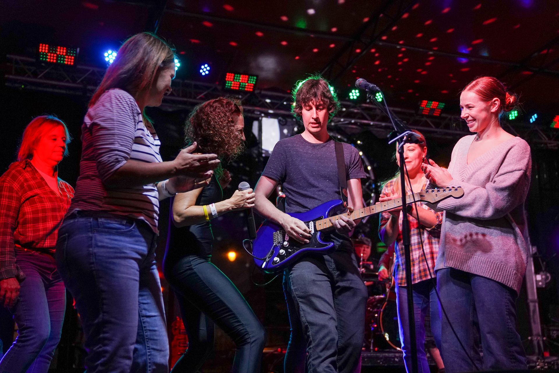 a group of people are standing around a man playing a guitar on a stage