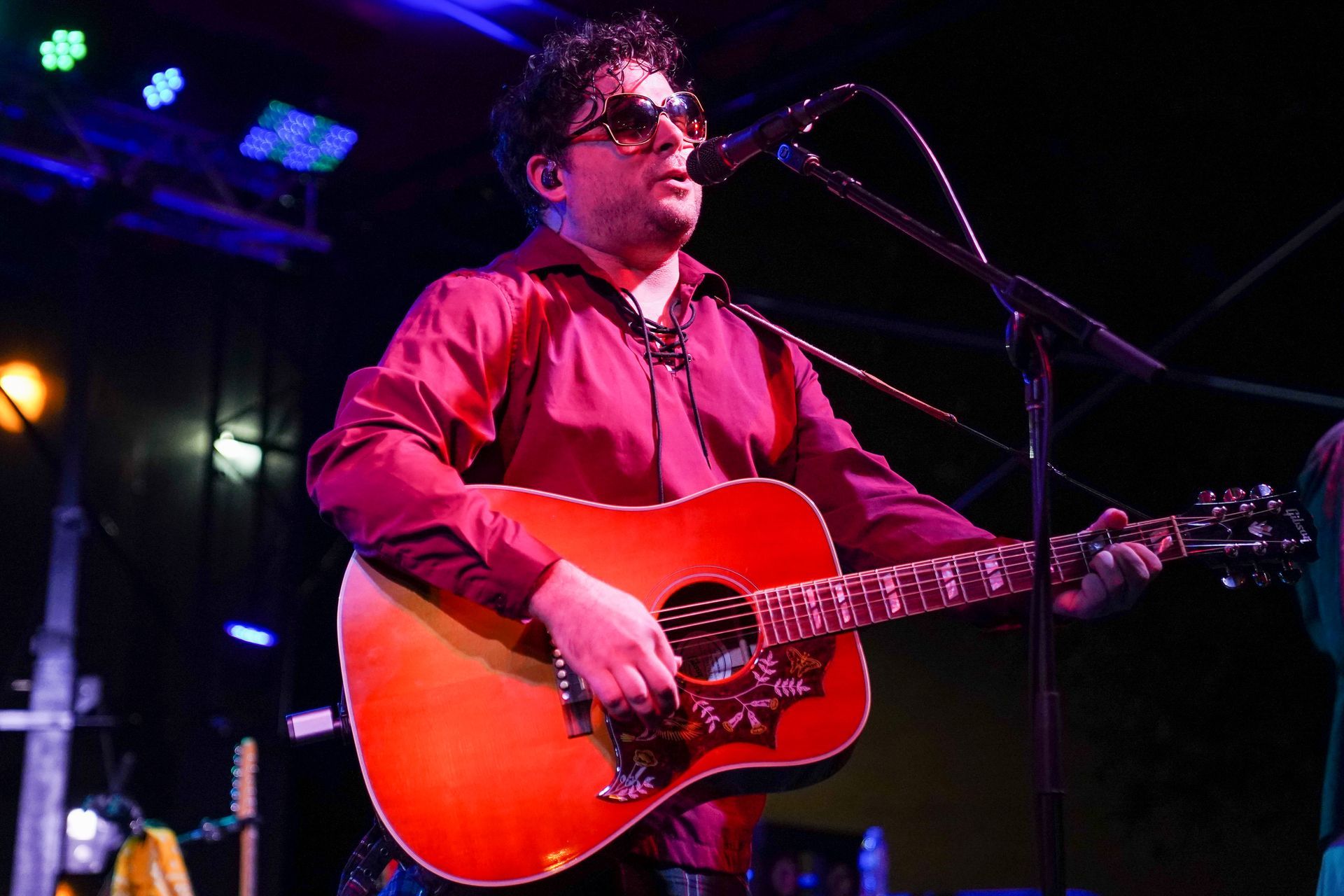 a man in a red shirt is playing an acoustic guitar and singing into a microphone