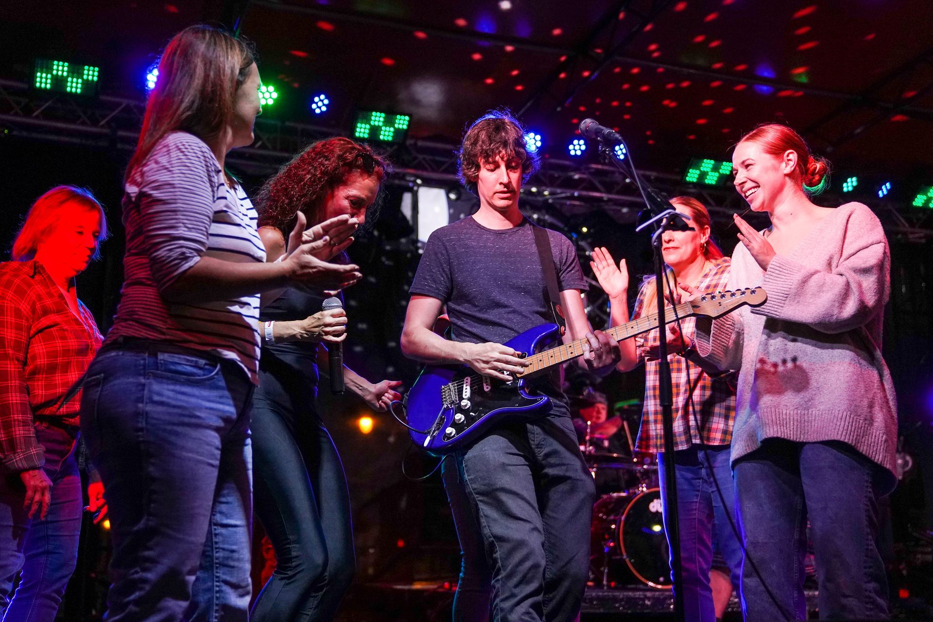 a group of people are standing around a man playing a guitar on a stage
