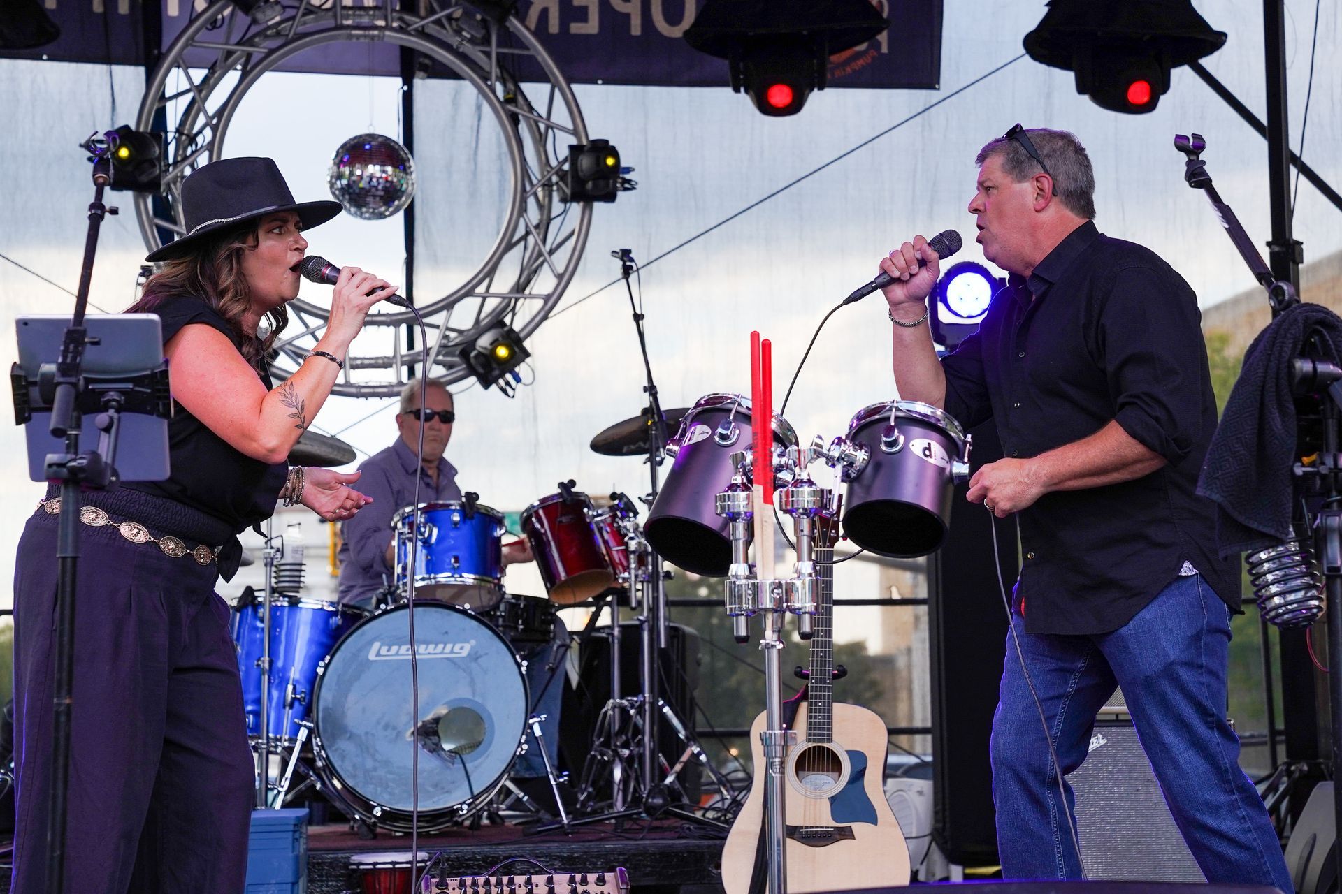 a man and a woman singing on a stage with drums in the background