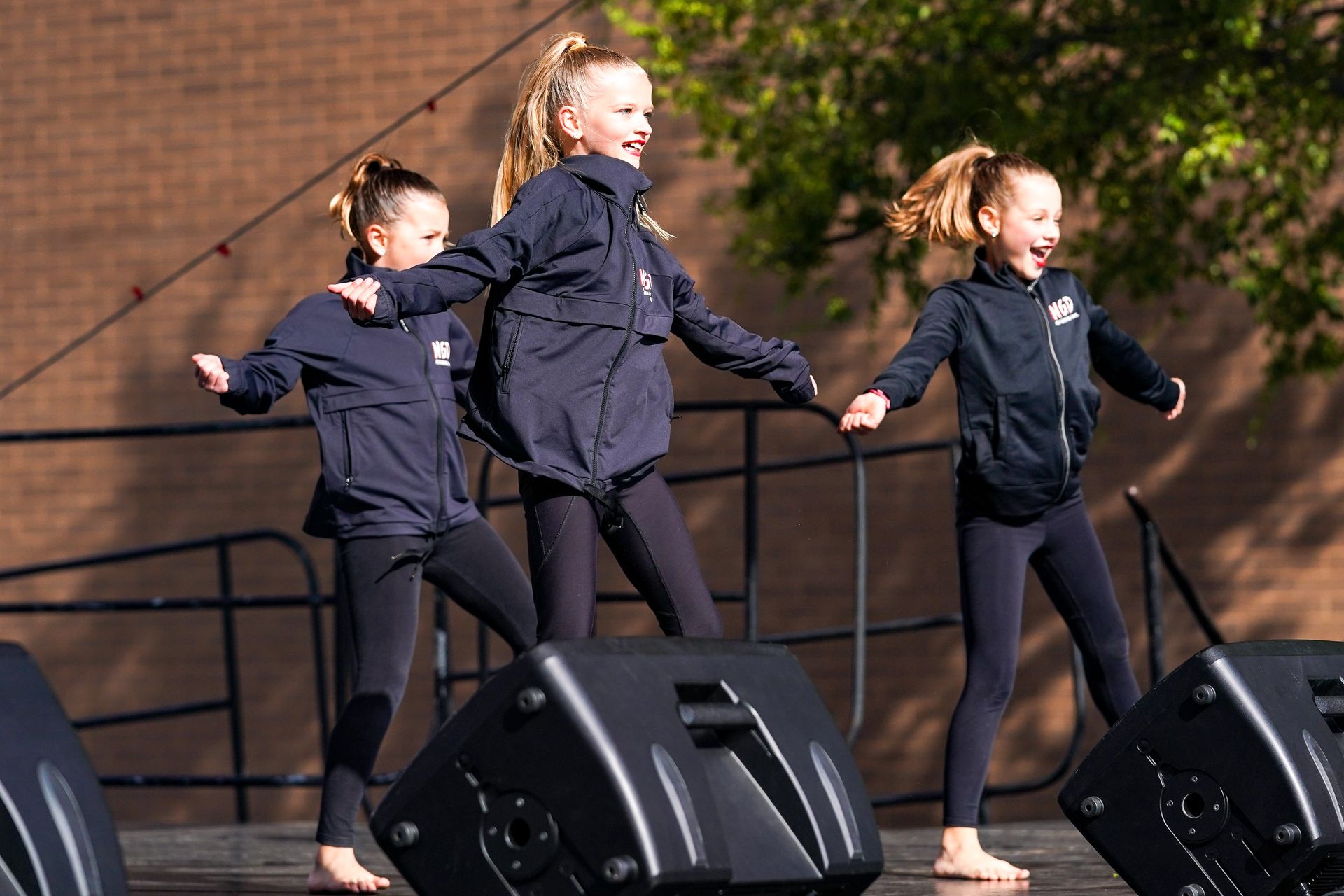 three young girls are dancing on a stage in front of speakers