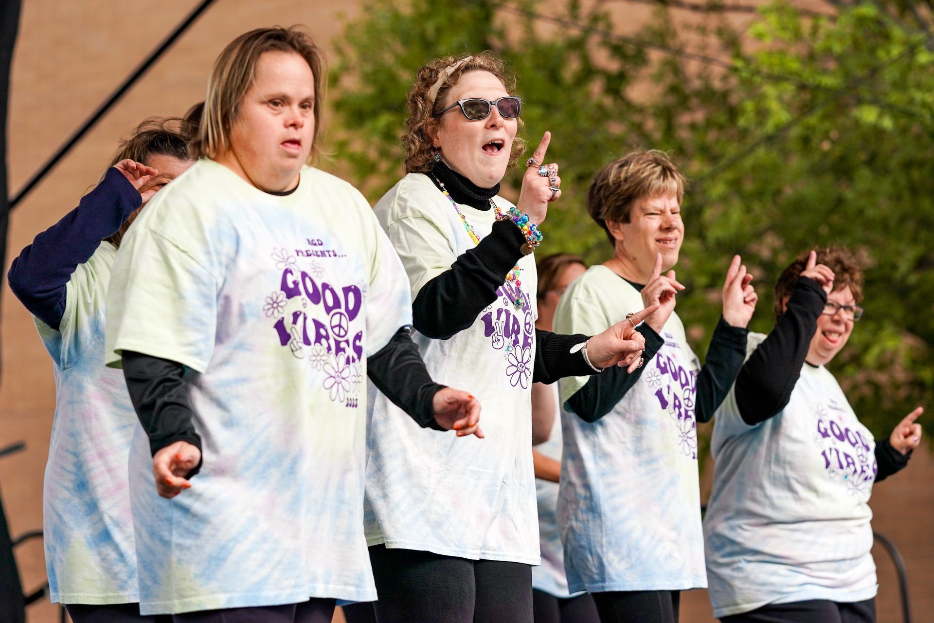 a group of women wearing tie dye shirts that say good vibes are dancing on a stage