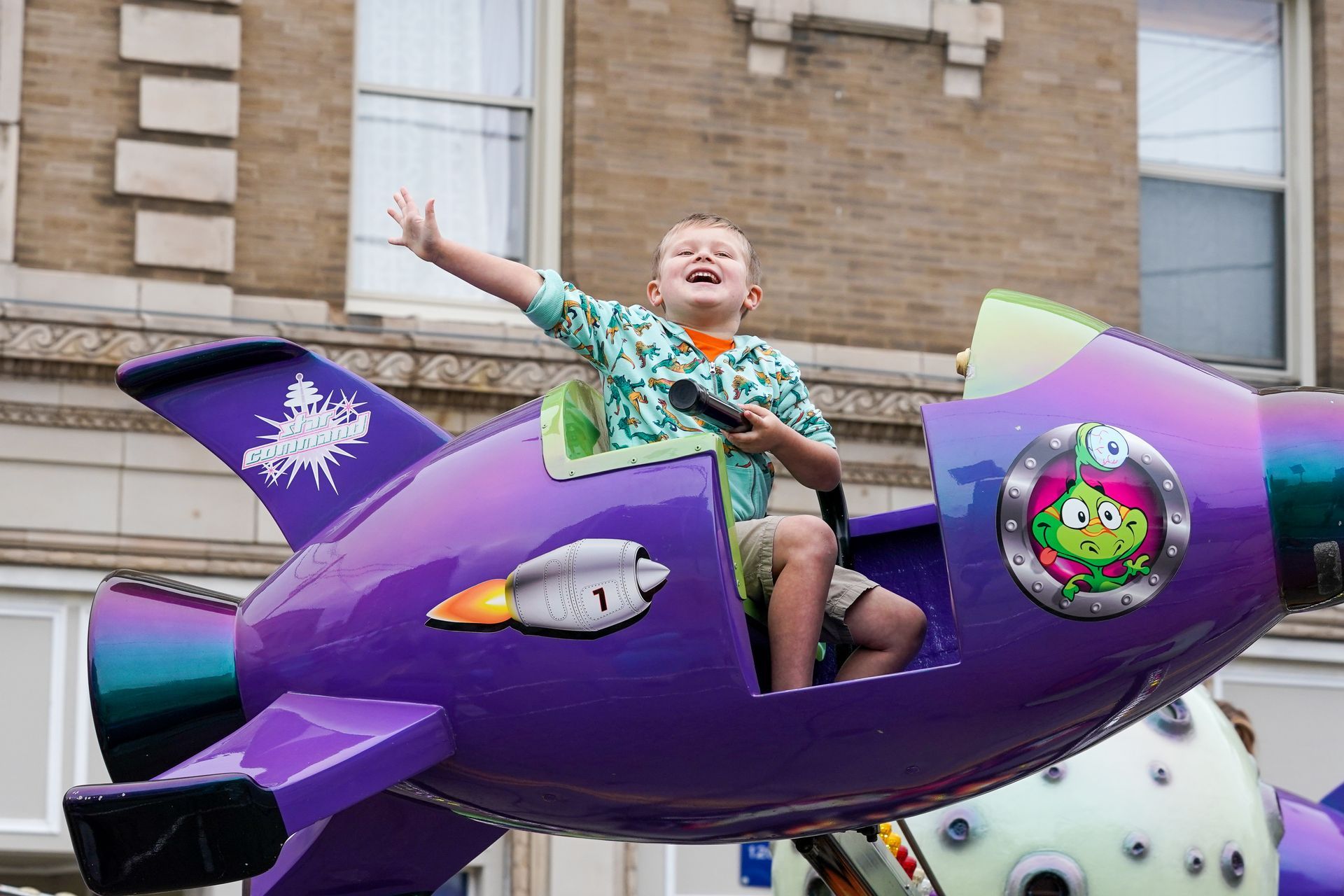 a young boy is riding a toy rocket in a parade