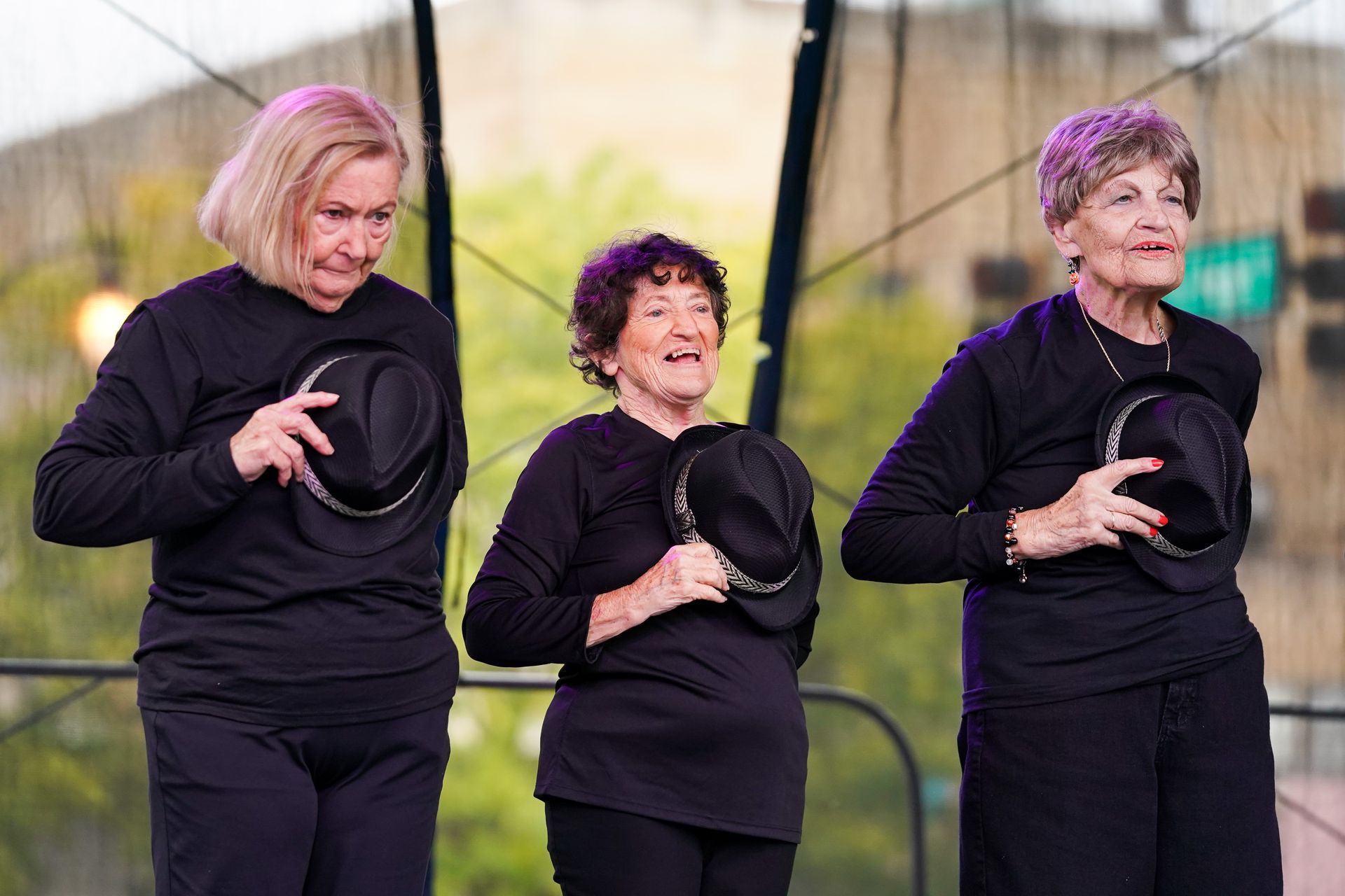 three older women wearing black shirts and hats are standing next to each other on a stage 