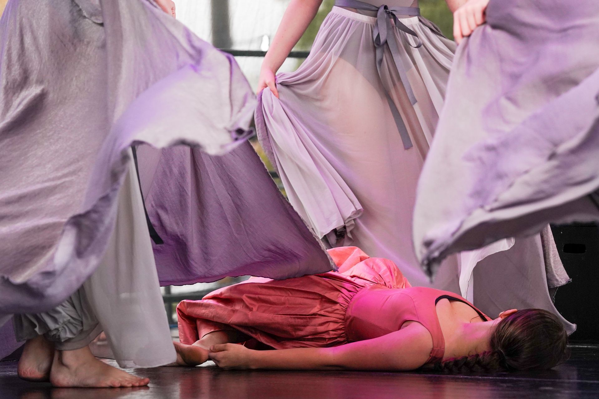 a woman in a pink dress is laying on the floor surrounded by other dancers
