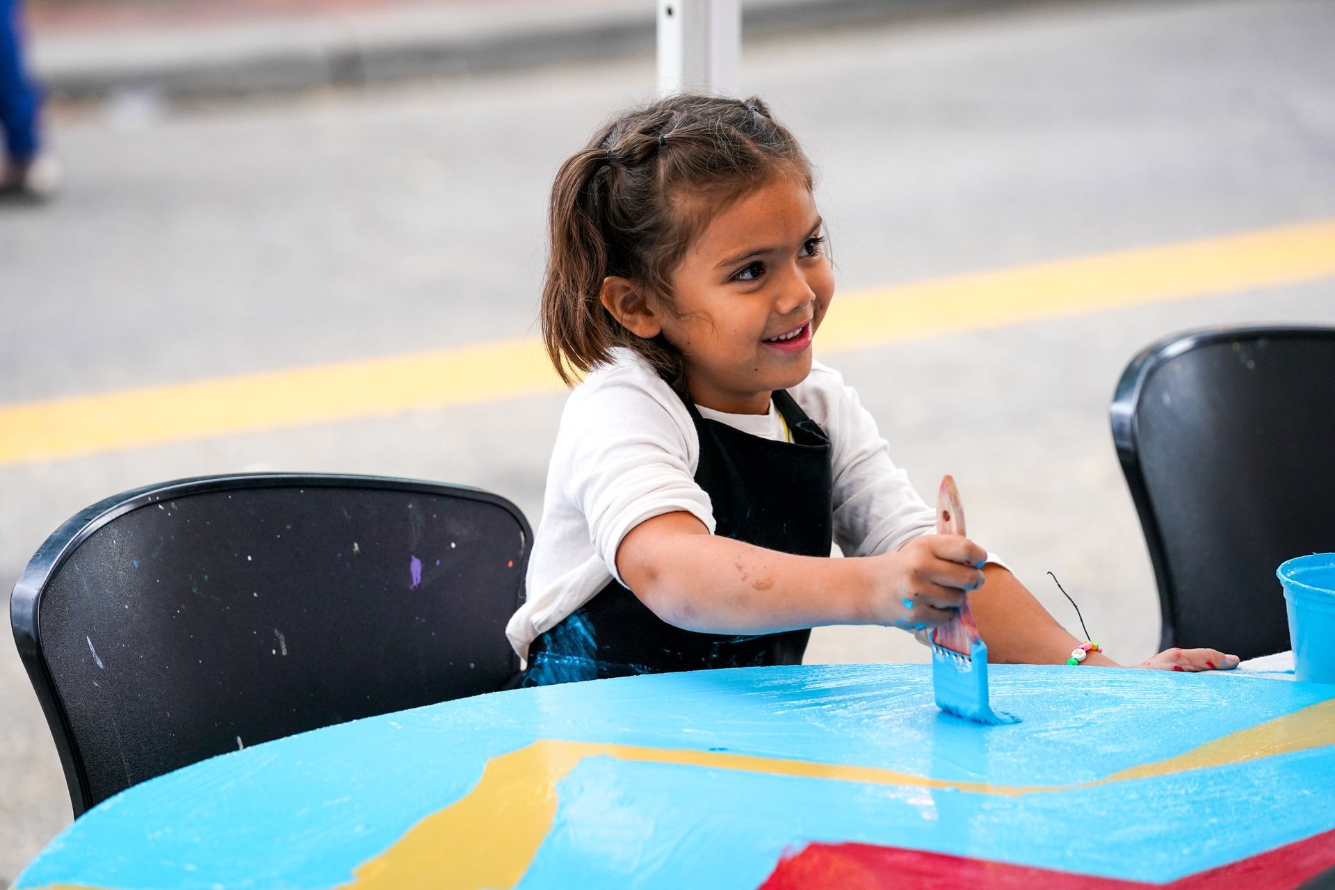 a little girl is sitting at a table painting with a brush