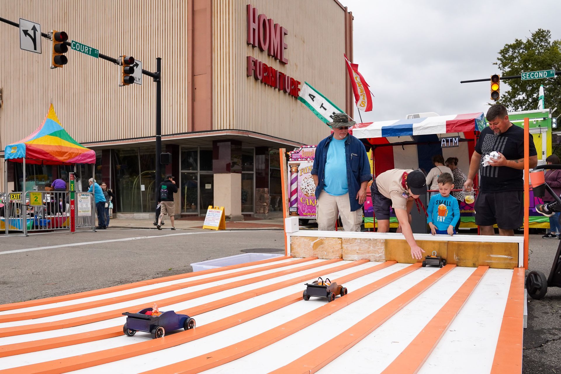 a man is playing with a toy car on a track in front of a building that says home furniture