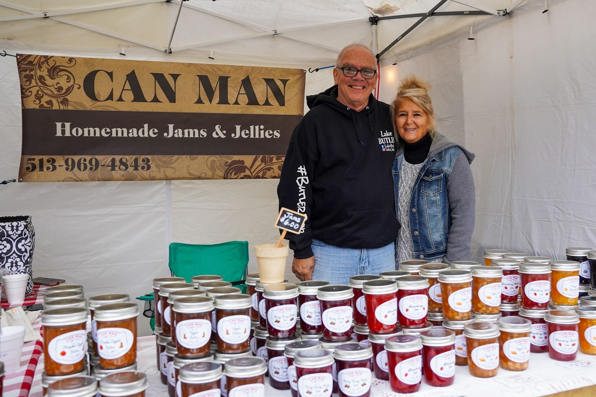 a man and a woman are standing in front of a table full of jars of jam