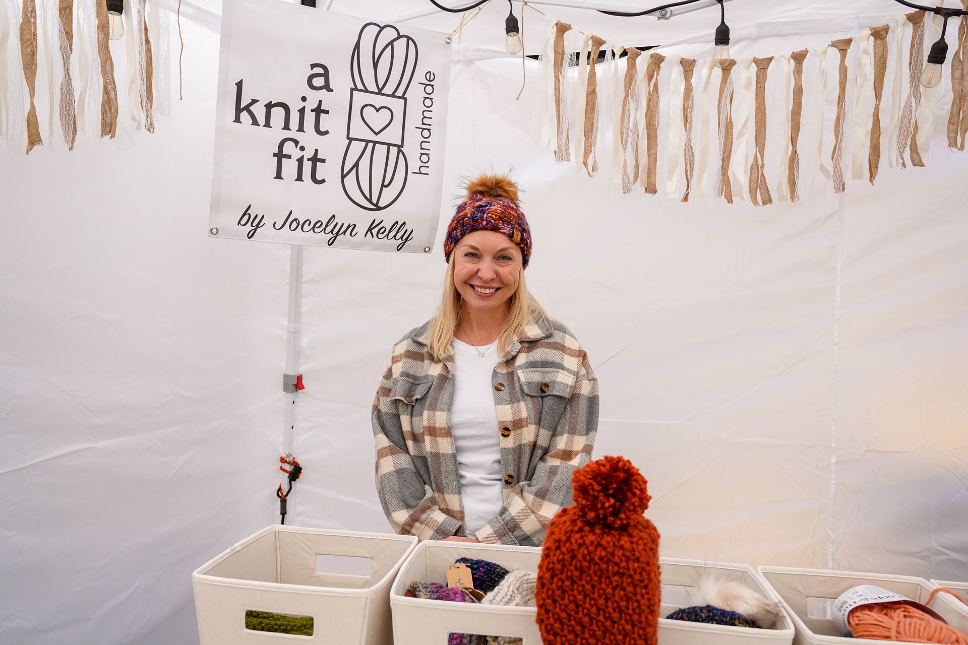 a woman is standing in front of a tent selling knitted items