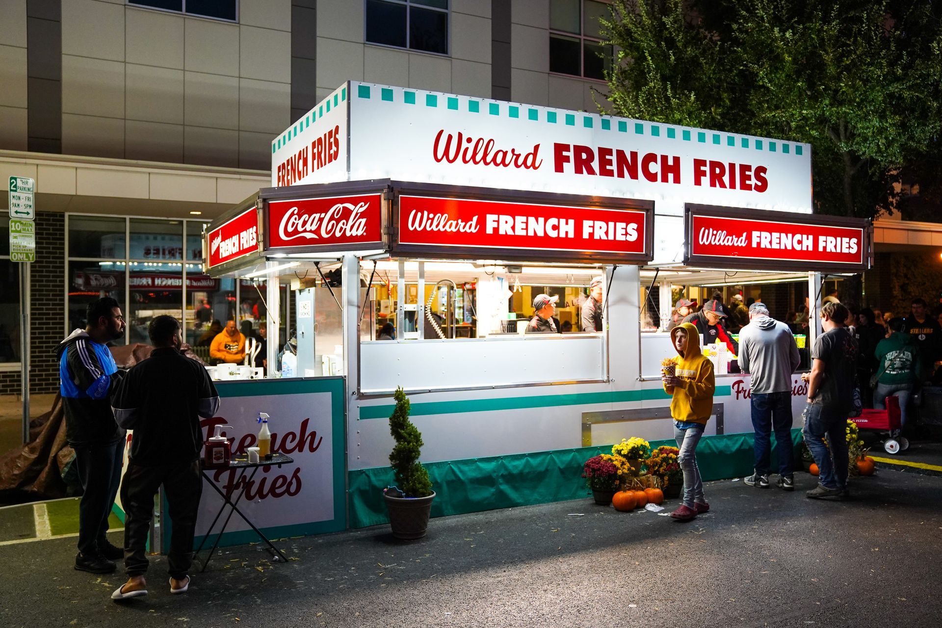 a group of people are standing around a french fries stand
