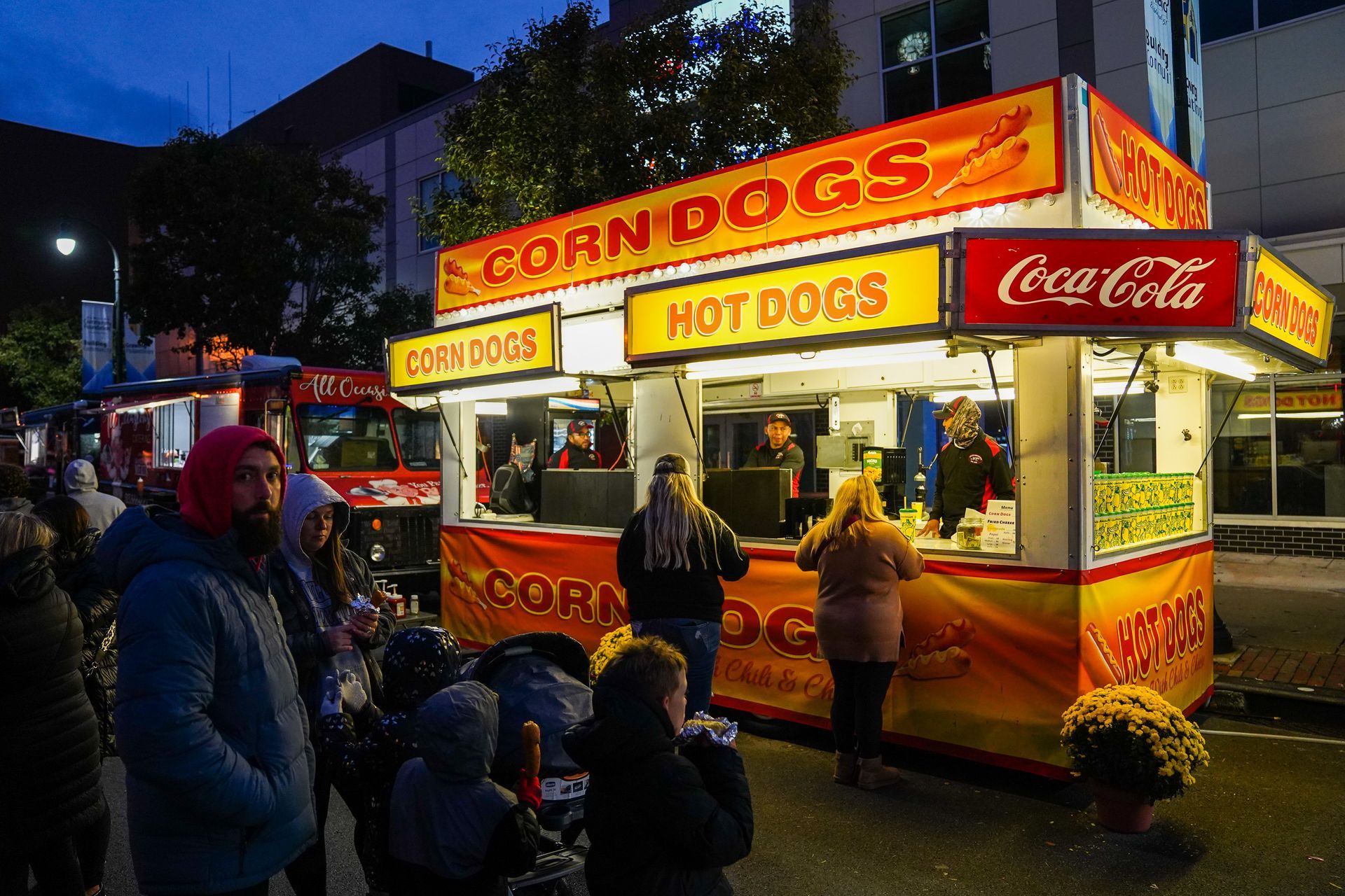a group of people are standing in front of a corndogs and hot dogs stand