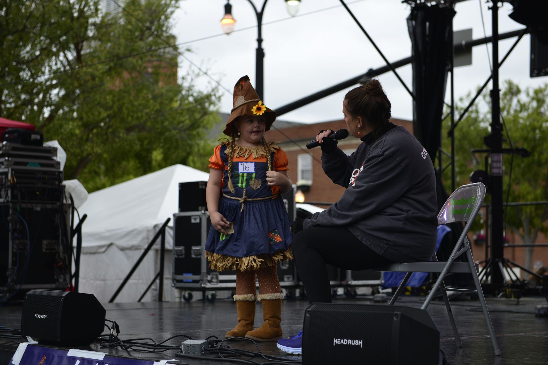 a little girl in a scarecrow costume is singing into a microphone on a stage