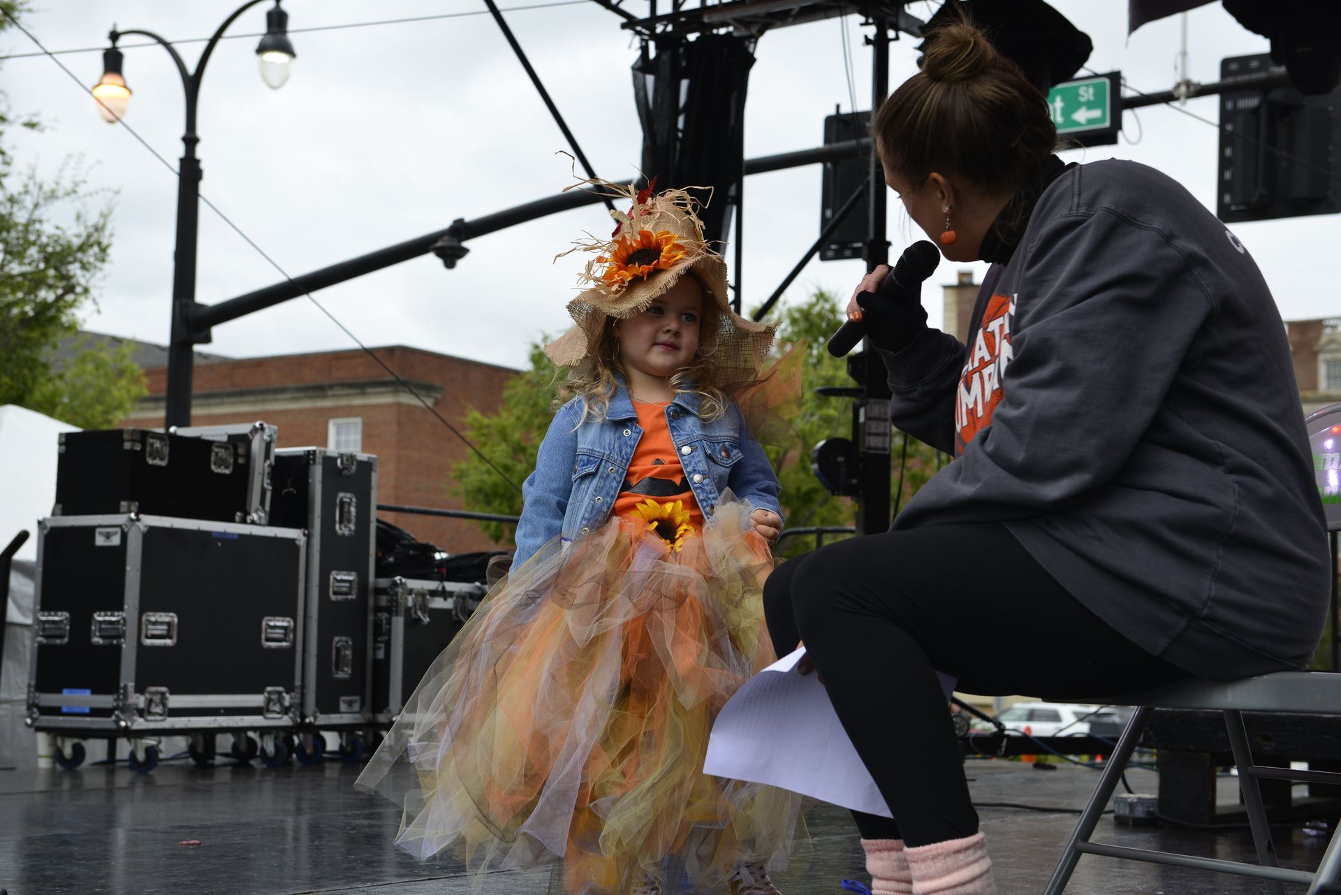 a woman is talking into a microphone while a little girl in a dress looks on