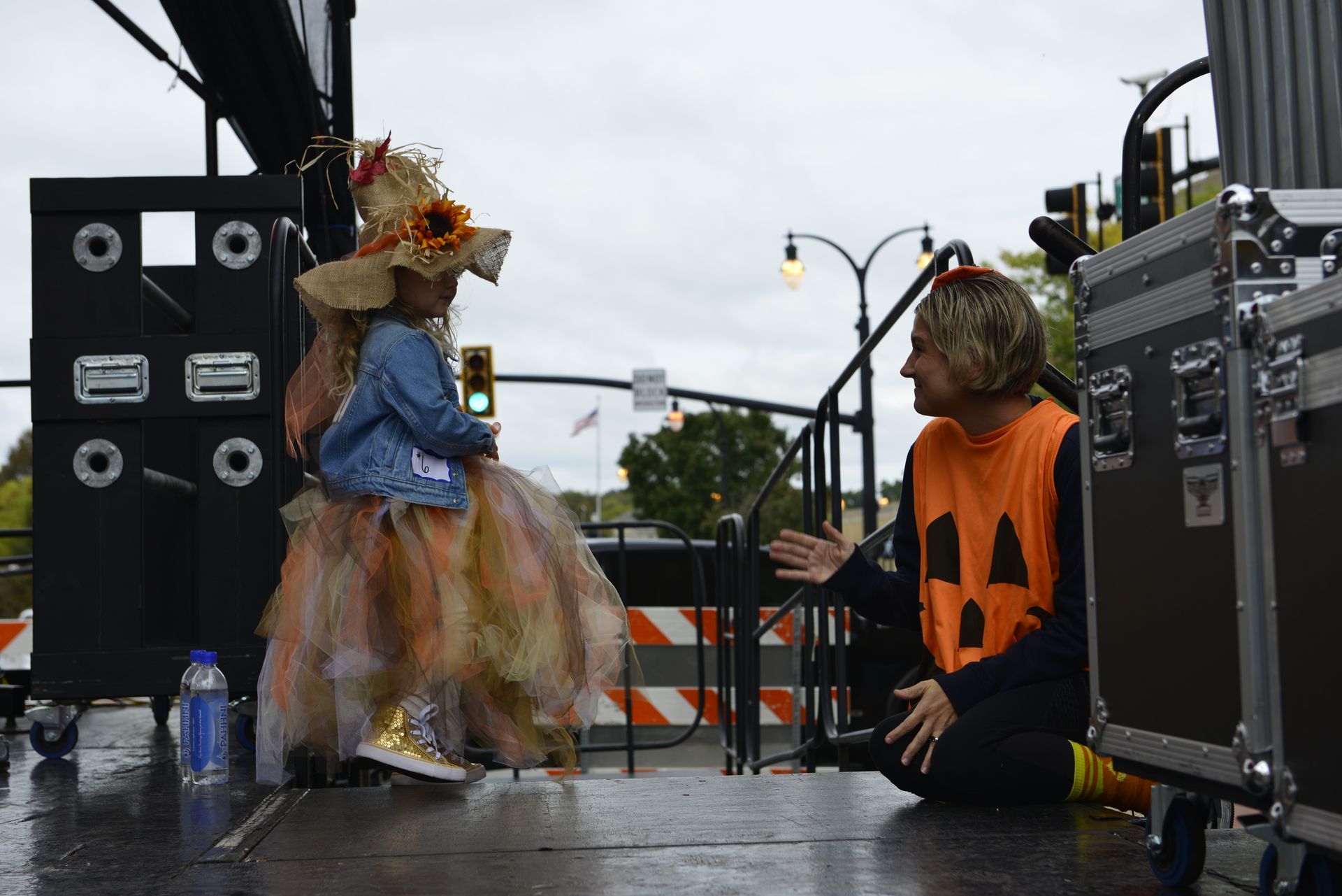 a man in an orange pumpkin vest talks to a little girl in a costume