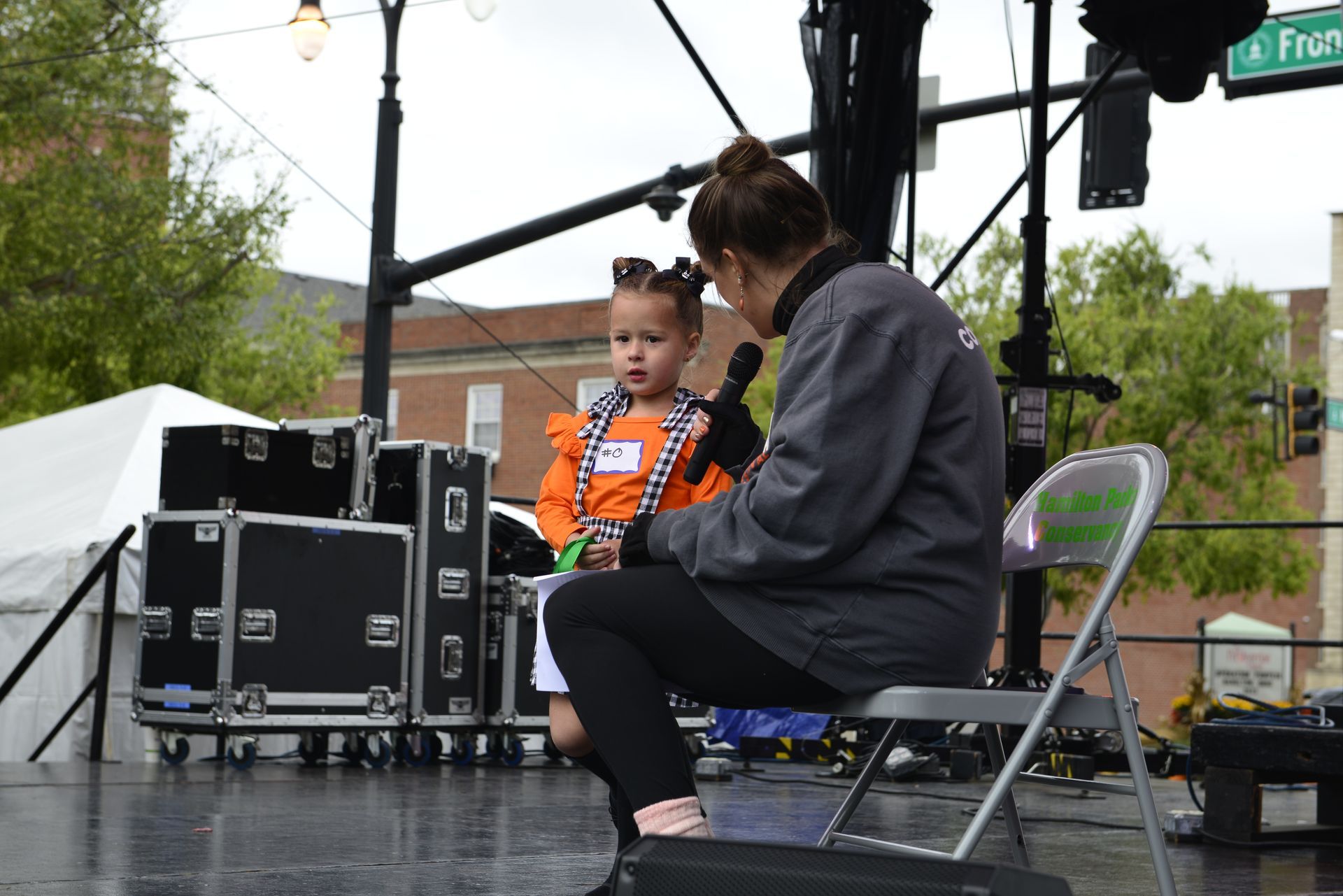 a woman is sitting on a stage talking into a microphone while a little girl looks on