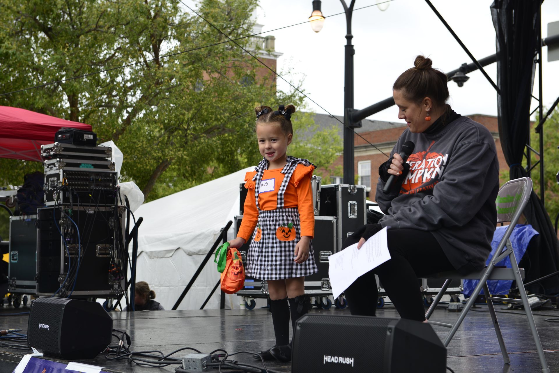 a woman is sitting on a stage talking to a little girl in a Halloween costume