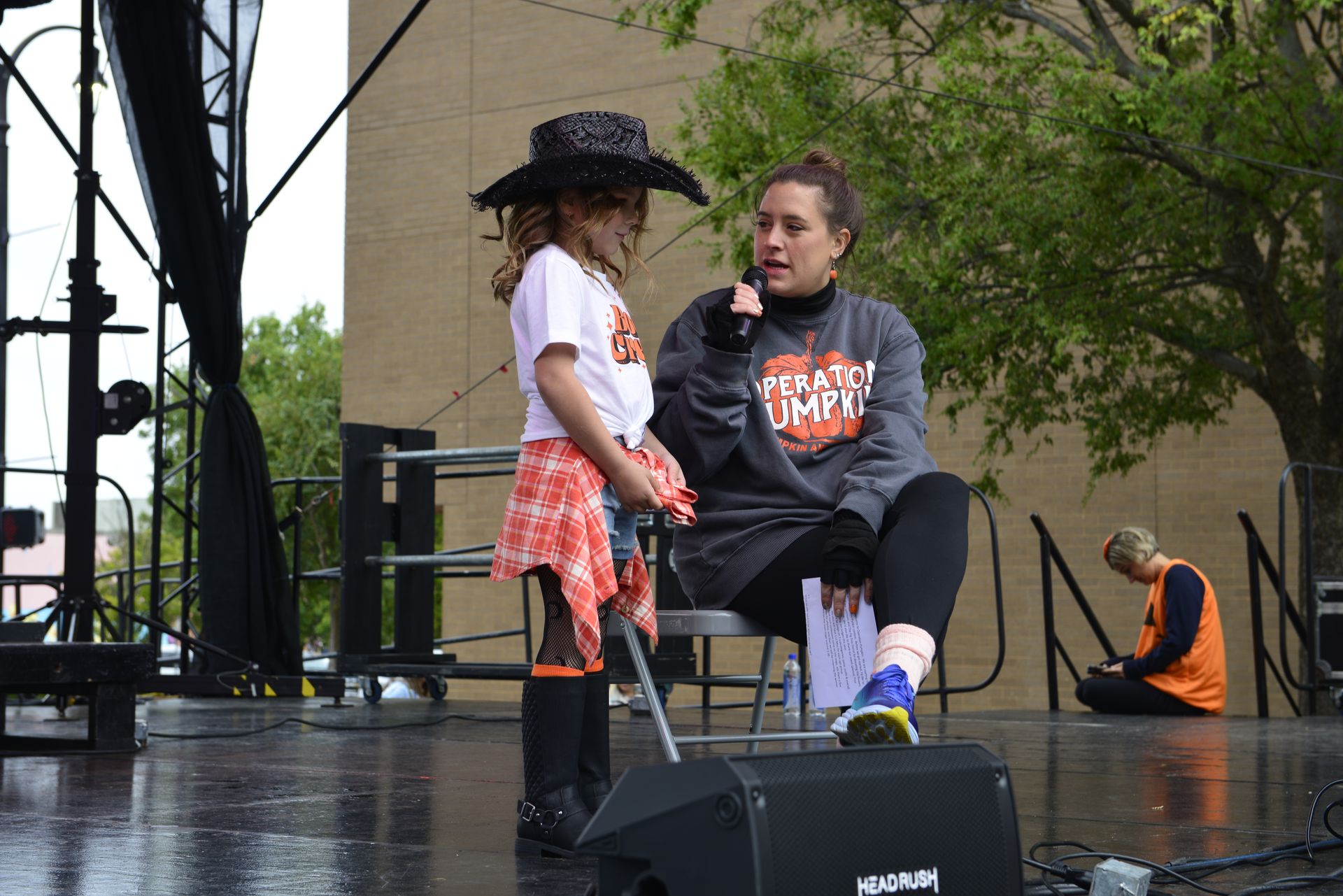 a woman is sitting on a stage talking to a little girl who is wearing a cowboy hat