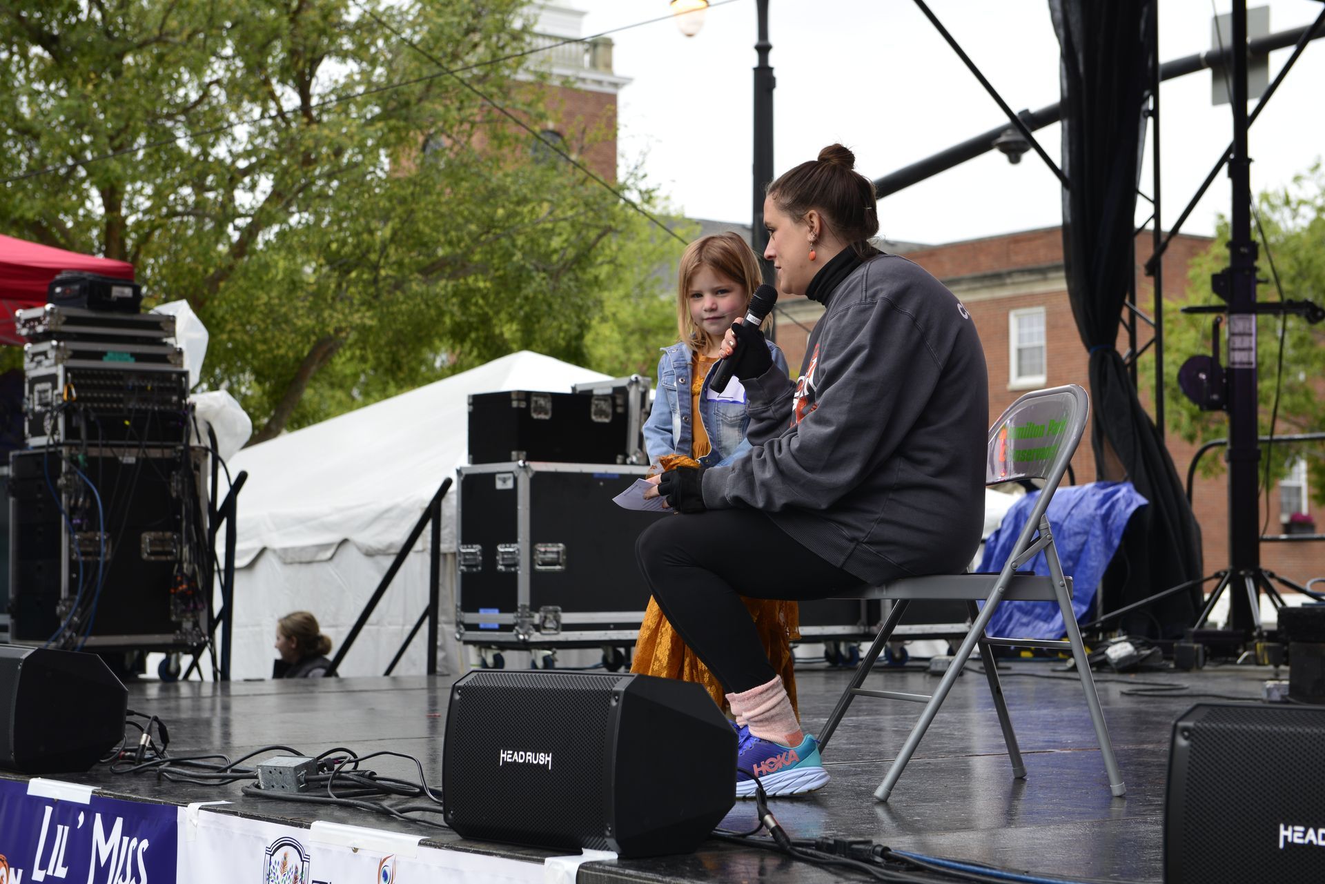 a woman is sitting on a stage talking to a little girl