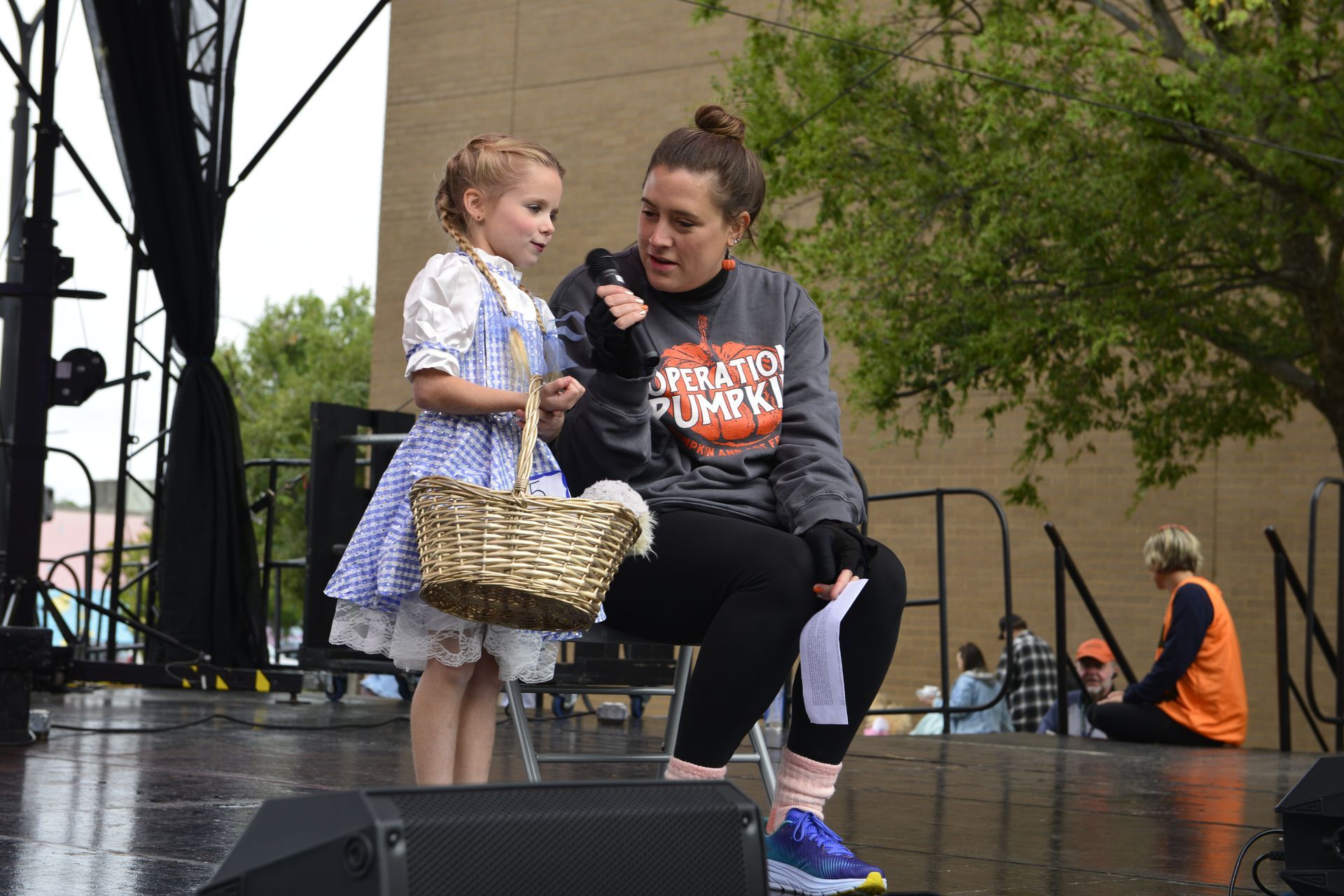 a woman is sitting on a stage talking to a little girl