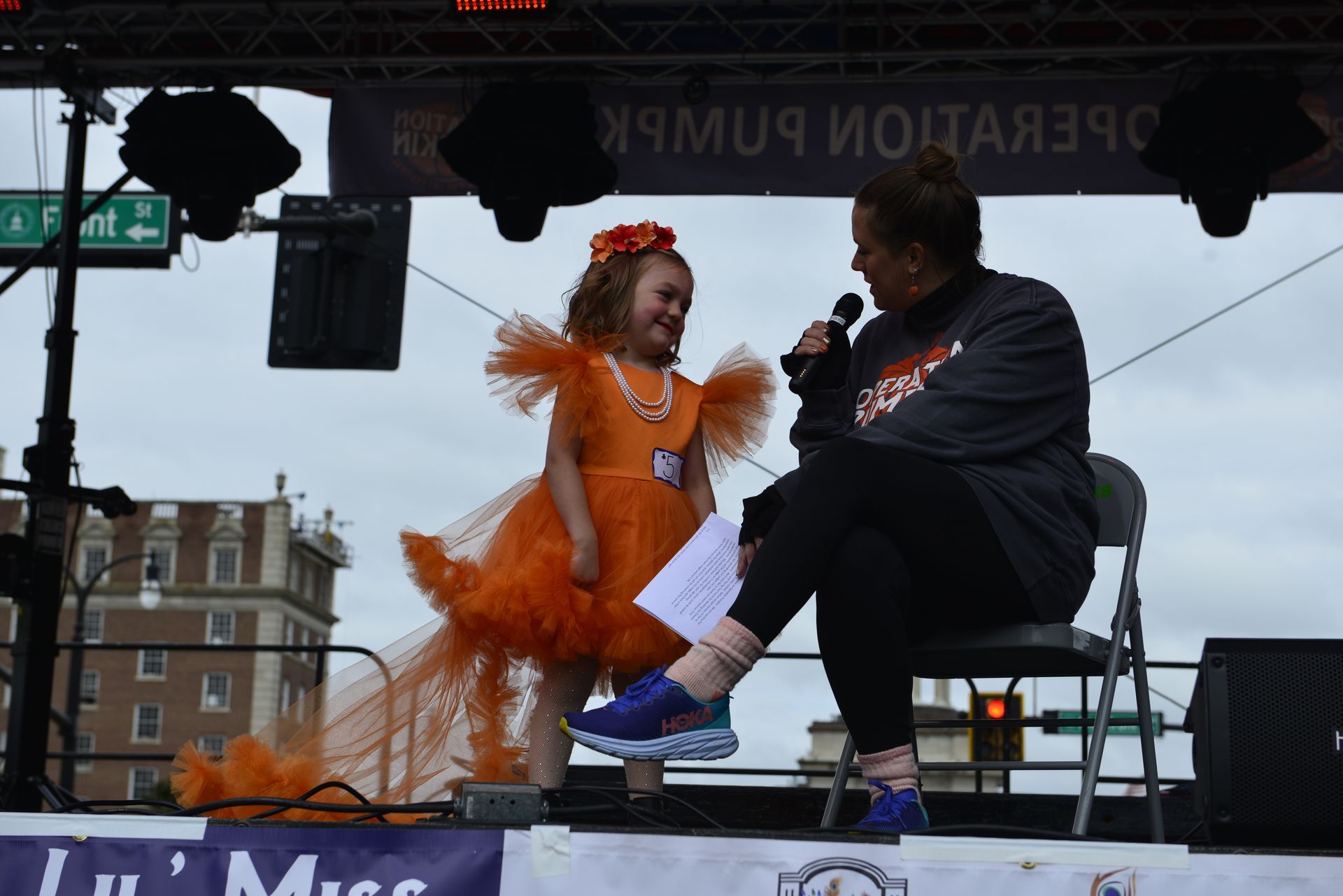 a little girl in an orange dress is standing next to a woman holding a microphone