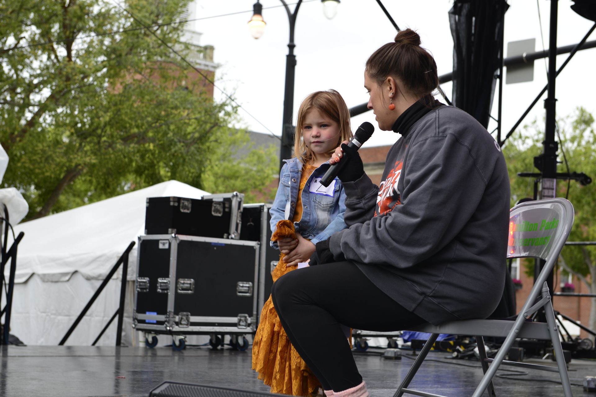 a woman is sitting on a stage talking to a little girl